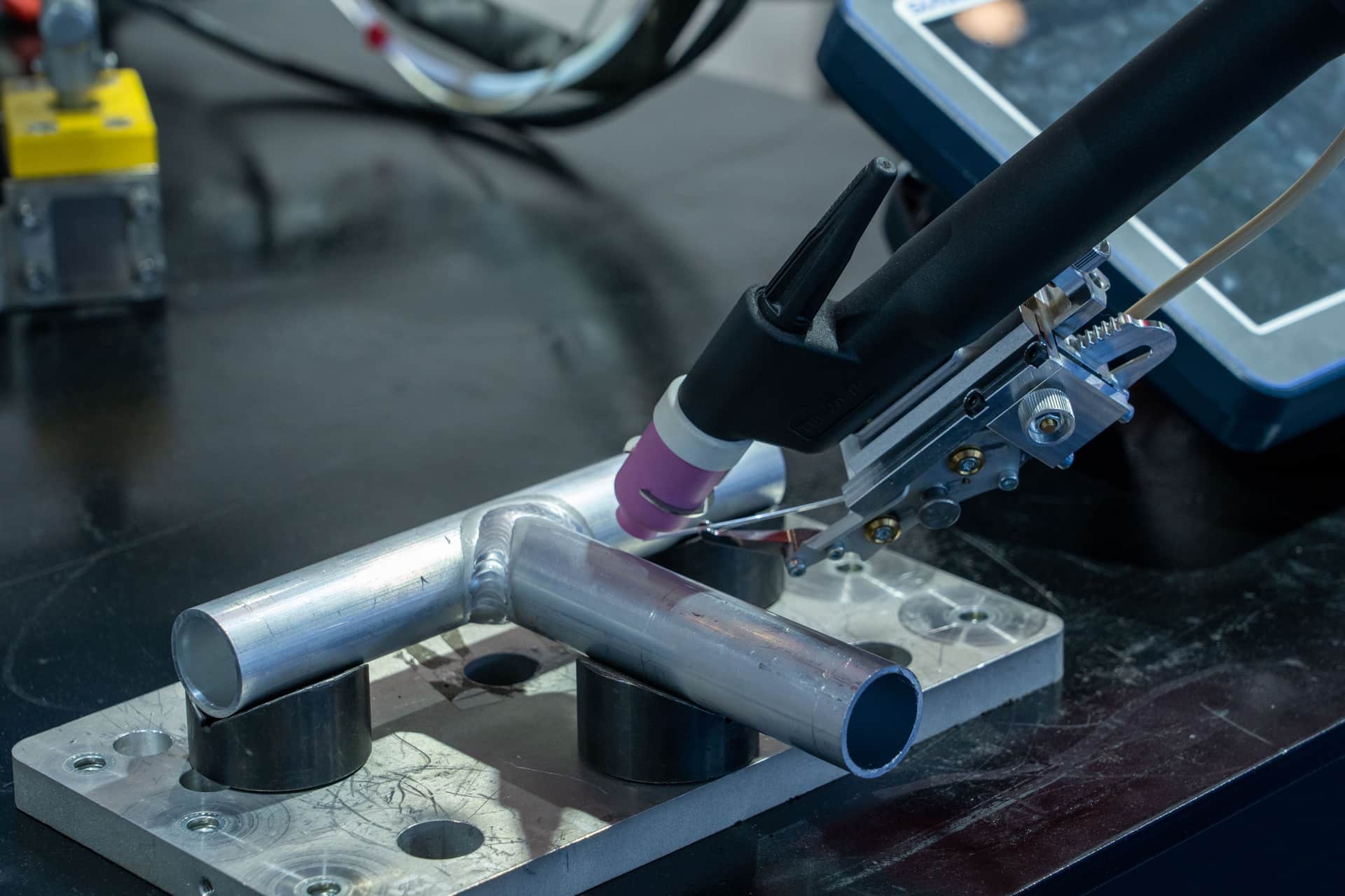 An AC/DC TIG welder with a foot pedal and torch coiled on a clean workbench